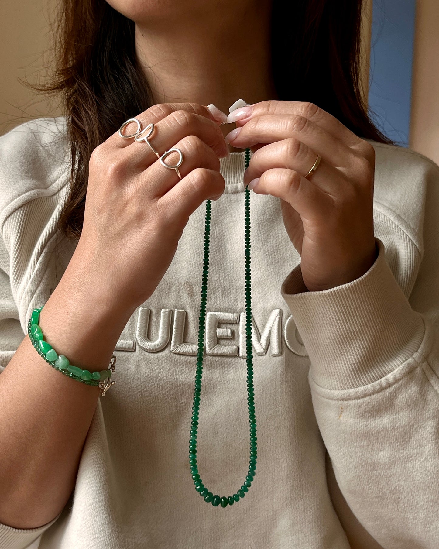 Person wearing a green beaded necklace and bracelet, with a neutral background
